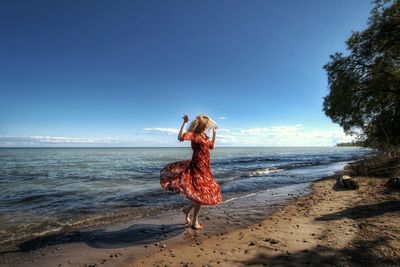 Woman dancing at beach against sky