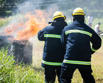 Rear view of firefighters standing against fire on field