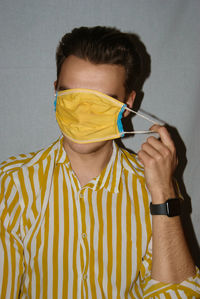 Portrait of man holding yellow umbrella against wall