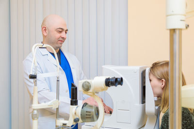 A male ophthalmologist checks the eyesight of a young girl using a modern vision tester