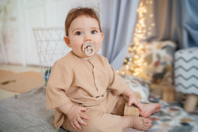 Baby with a pacifier in his mouth sits on the floor