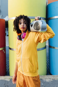 Woman carrying boom box on shoulder standing in front of colorful pipes