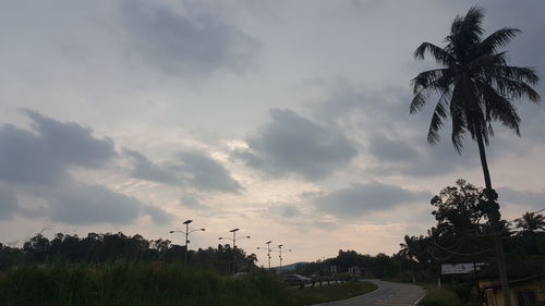 Road by trees against sky during sunset