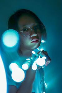 Young woman with illuminated string lights standing at home