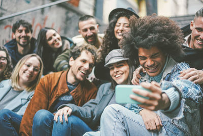 Cheerful man taking selfie with friends while sitting outdoors