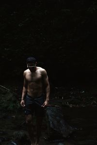 Rear view of shirtless man standing in forest