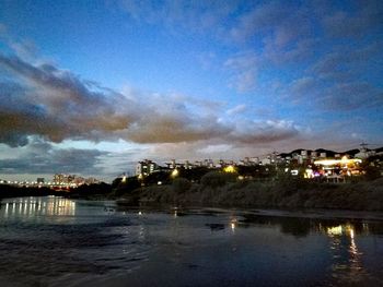 Illuminated city by sea against sky