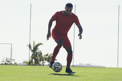 Full length of african american soccer player playing on grass pitch