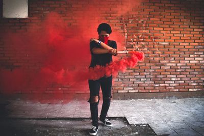 Full length of man holding distress flare while standing against brick wall