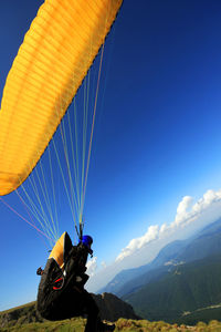 Paraglider with parachute on mountain against blue sky