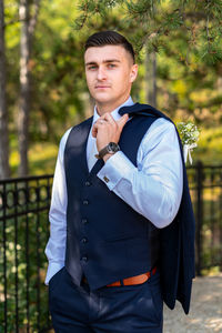 Handsome young groom wearing elegant dark blue suit looking at camera outdoors portrait. 
