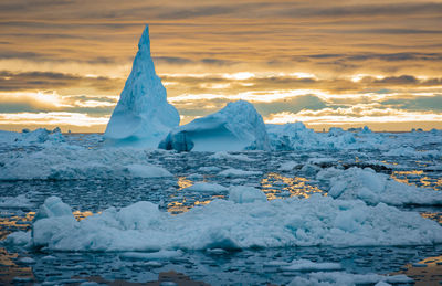 Icebergs at beach against sky during sunset
