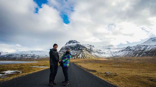 Portrait of couple standing on road against snowcapped mountains