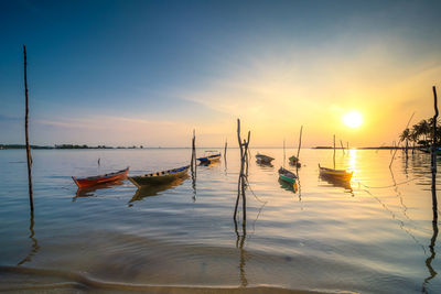 Boats moored in sea against sky during sunset