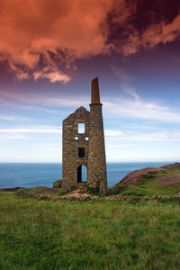 Old building on field by sea against sky