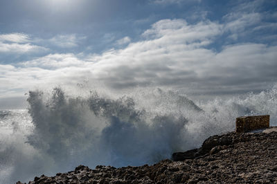 Sea waves splashing on rocks against sky