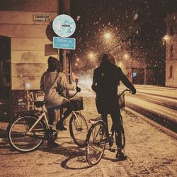 Rear view of people cycling on street at night during winter