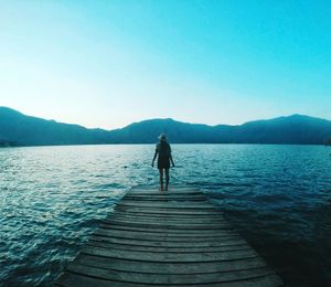 Rear view of woman standing on pier over lake against clear sky