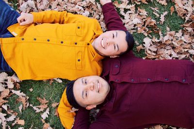 Portrait of smiling young friends lying on leaves covered field during autumn