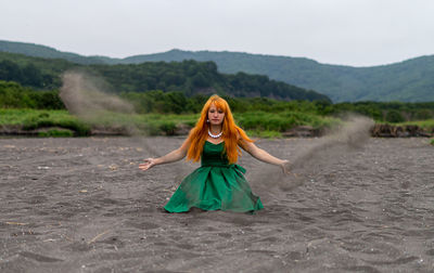 Woman playing with sand at beach against sky