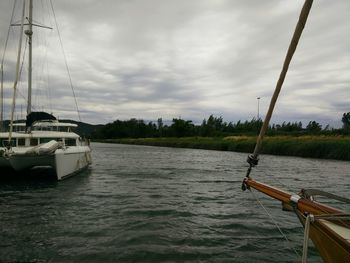 Boats in river against cloudy sky