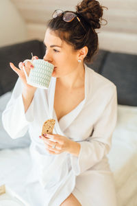 Young woman having coffee while sitting on bed at home