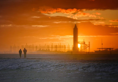 Silhouette people on beach against sky during sunset