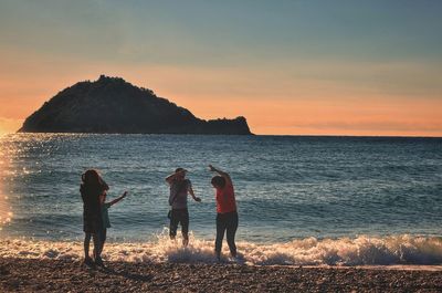 Men standing on beach against sky during sunset