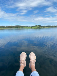 Low section of person by lake against sky