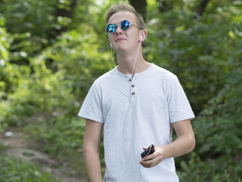 Young man with headphones standing in forest