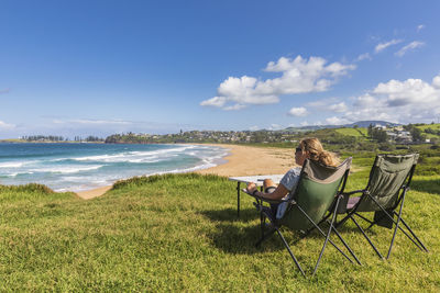 Man sitting on chair by sea against sky