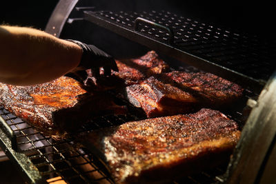 From above of crop chef in gloves grilling chunks of meat in on rack in barbecue