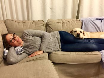 Portrait of woman lying with labrador retriever on sofa at home