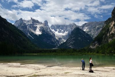 Men on lake by mountains against sky