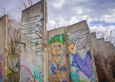 Low angle view of graffiti on berlin wall against cloudy sky