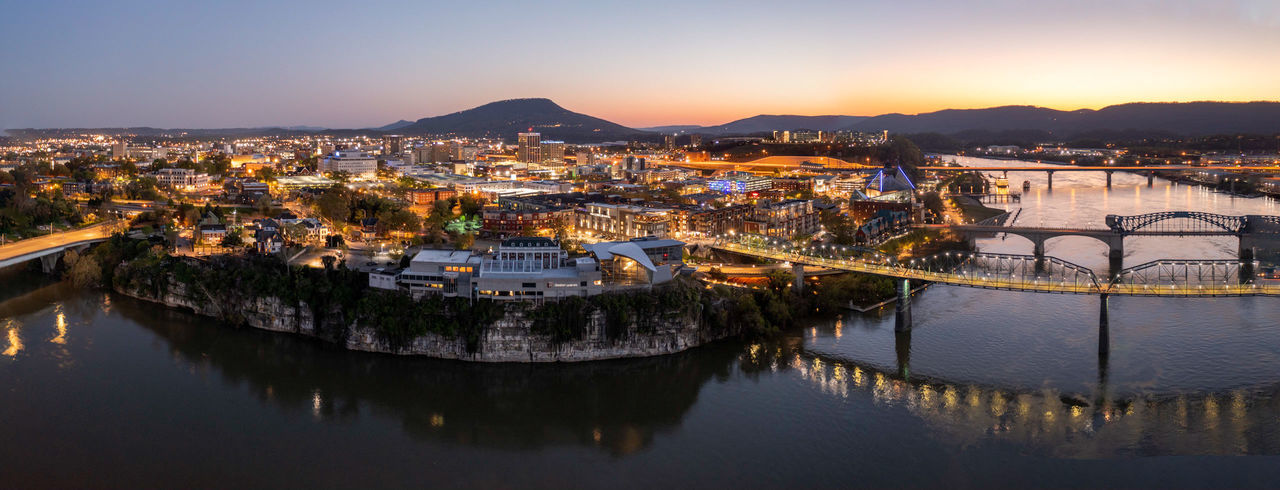 HIGH ANGLE VIEW OF ILLUMINATED BUILDINGS BY RIVER AGAINST SKY