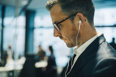 Side view of mature businessman with eyeglasses wearing headphones at office