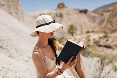 Woman reading book while sitting on rock formation