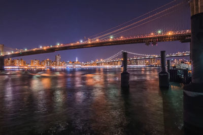 Illuminated bridge over river against sky at night