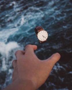 Cropped hand reaching wristwatch over sea