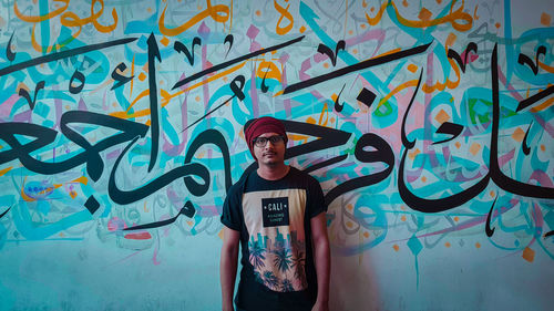 Portrait of young man standing against graffiti wall