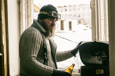 Side view of man standing with bottle by barbecue