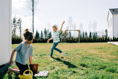 Boy dancing around the garden playing whilst his sister plants seeds