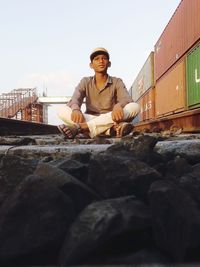Portrait of young man sitting on rock against sky