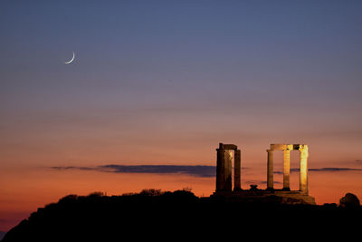 Silhouette factory by building against sky during sunset and moon