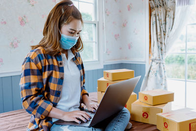 Asian woman at home using laptop to sell products online.