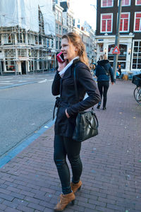 Full length of young woman using mobile phone on street