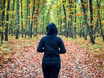 Back of woman wearing black tracksuit with hoodie standing alone in the middle of the forest