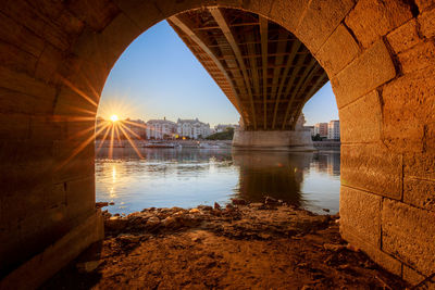 Arch bridge over river in city against sky during sunset