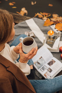 High angle view of woman holding coffee cup sitting on pier by lake